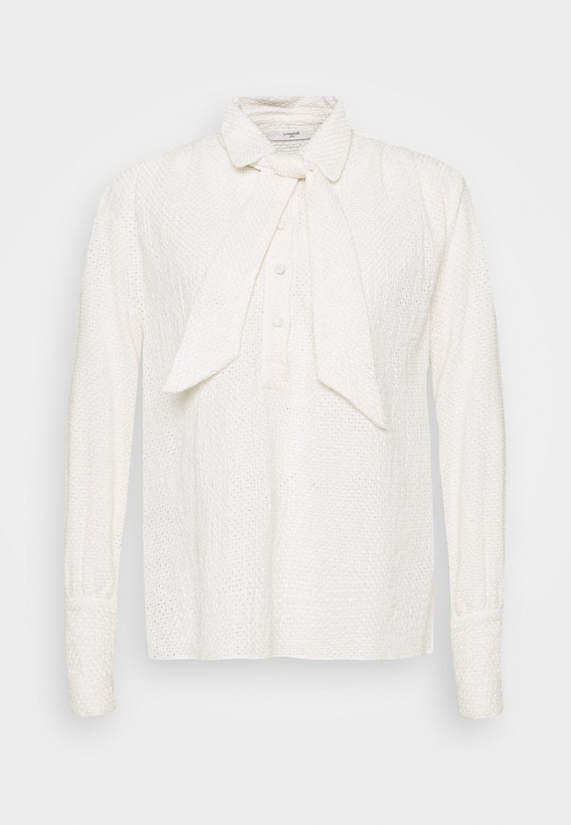Blouse blanche texturée à manches longues, fermeture boutonnée à l’avant, grand col et détail cravate attaché sur fond uni.