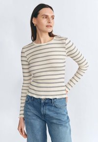 Długi rękaw, prążkowana bluzka w kolorze kremowym z granatowymi poziomymi paskami. Okrągły dekolt, dopasowany krój, w zestawie z wysokim stanem niebieskich dżinsów.