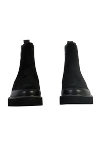 Bottines Chelsea en daim noir avec des bordures en cuir lisse, des panneaux latéraux élastiques et une semelle en caoutchouc épaisse et texturée.