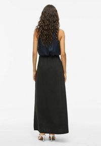 Robe maxi avec un haut bleu marine foncé et une jupe noire. Tissu lisse avec une taille cintrée, dotée de bretelles spaghetti et d'un design fluide. Talons argentés.