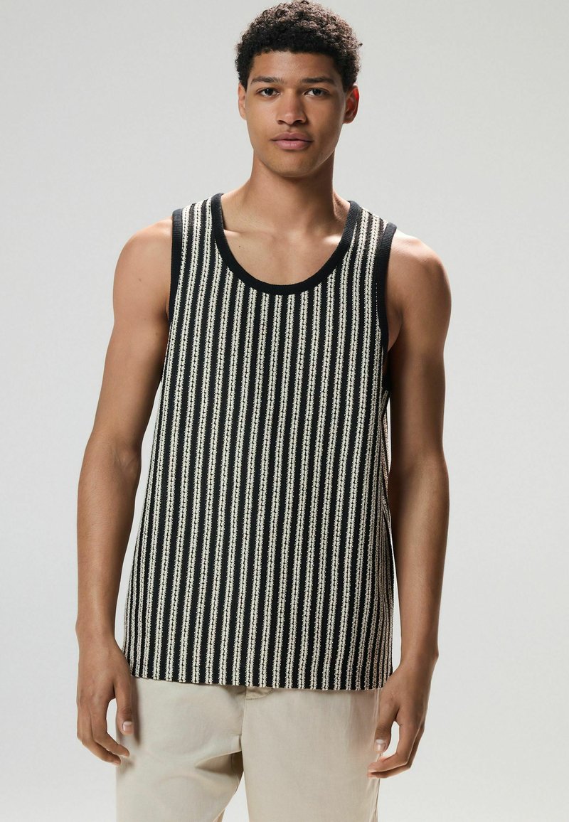 Gestreiftes Tanktop in Schwarz-Weiß aus Strickstoff, mit weiten Armausschnitten und Rundhalsausschnitt, kombiniert mit hellen Hosen.