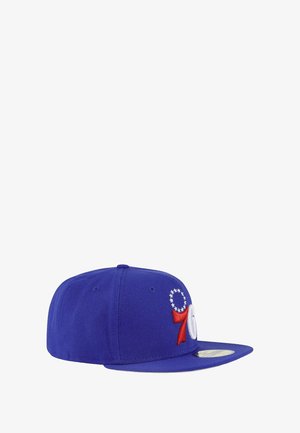 Blauwe snapback pet met geborduurde witte en rode logo's, steraccenten en een platte rand. Gemaakt van duurzaam materiaal.