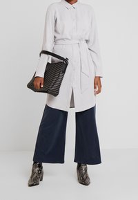Abito camicia lungo grigio chiaro con colletto e bottoni, cintrato in vita. Abbinato a pantaloni larghi blu navy e stivali con tacco in stampa serpente nera.
