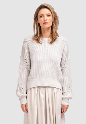 Jasnoszara sweter z dzianiny o prążkowanej fakturze, z opadającymi rękawami i dekoracyjnymi detalami w formie oczek. Połączony z zwiewną beżową spódnicą.