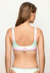 Bralette in gradiente pastello con spalline larghe, texture liscia e una fascia con dettagli dorati nella parte inferiore. La vista posteriore mette in mostra un collo rotondo.