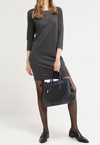 Czarna i granatowa torebka na rękę z podwójnymi uchwytami, gładką teksturą i strukturalnym designem. Noszona z szarym sukienką i czarnymi rajstopami, prezentująca błyszczące buty.