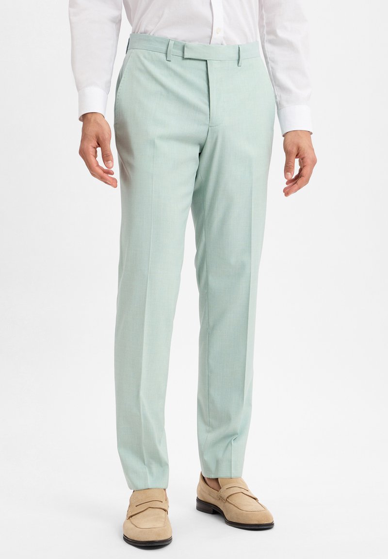 Lichtgroene op maat gemaakte broek van een gladde stof, met een platte voorkant, twee zijzakken en een slanke pasvorm, gecombineerd met beige loafers.