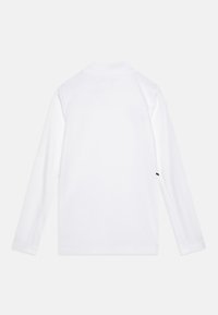 Chemise blanche à manches longues avec col, coutures et accents sur les côtés. Texture lisse avec une coupe régulière et sans motifs visibles.