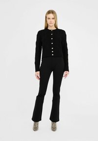 Zwarte gebreide cardigan met kabelpatroon, voorzien van parelknoopjes. Gecombineerd met zwarte uitlopende broek en enkellaarsjes met slangenprint.