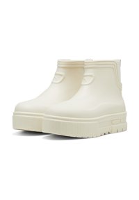 Bottes de cheville imperméables de couleur crème avec une texture lisse, semelle plate et bout arrondi. Présente un logo discret sur les côtés.