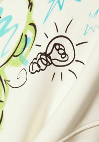 Tela color crema que muestra una impresión gráfica de una bombilla con un boceto a mano, rodeada de garabatos y acentos en verde y azul.