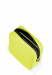 Neon gele toilettas met een glanzende afwerking, rechthoekige vorm, zwarte ritssluiting en een logo-geprinte trekker. Soepele textuur.