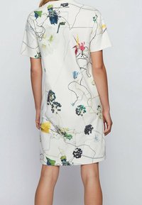 Blommönstrad kortärmad klänning i vitt, med färgglada blommor och växtillustrationer med svarta linjekonturer. Avslappnad och löst sittande design.