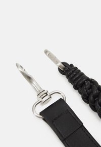 Schwarzes Lederarmband mit geflochtenem Muster, ausgestattet mit einem silbernen Metallclip und -ring. Klare Markenkennzeichnung auf dem Metallteil.