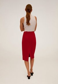 Jupe crayon rouge avec une fente à l'arrière, associée à un haut sans manches ajusté blanc. Texture de tissu lisse et design simple.