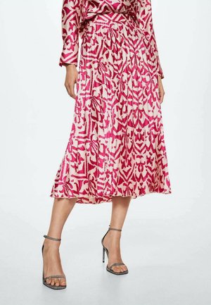Mujer con falda midi plisada con estampado en rosa y rojo, blusa a juego y sandalias plateadas de tacón alto.