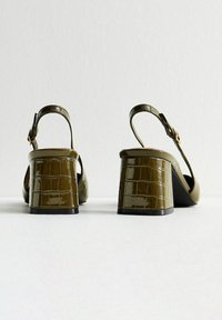 Sandali verde in pelle verniciata con tacco a blocco, texture coccodrillo, design slingback e chiusura con fibbia regolabile.