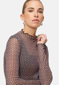 Haut transparent à manches longues avec une base noire ornée d'un motif de losanges roses et blancs. Agrémenté d'un col et de poignets à volants.