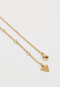 Goudkleurige ketting met een driehoekige hanger met reliëfmerklogo, en een kreeftsluiting voor het vastmaken.