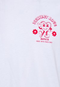 Camiseta blanca de algodón con un gráfico de un personaje de corazón de dibujos animados, texto rosa "AMOR PERFECTO" y acentos de flores.