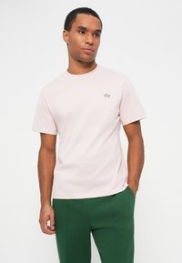 Rožinė trumpomis rankovėmis T-shirt iš medvilnės, su apvaliu kaklu ir mažu žaliu krokodilo logotipu kairėje krūtinės pusėje.