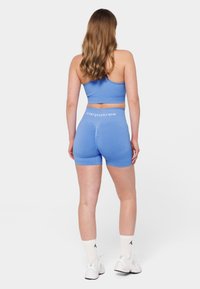 Sinine sportlik lühike top ja lühikesed püksid, mis on valmistatud venivast kangast, sisaldavad lühikeste pükste kokkurugete detaili ja logo vööl.
