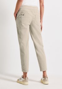 Pantalon beige court avec taille élastique, deux poches arrière et une texture lisse, associé à des baskets de couleur claire.