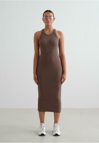 Brown ribbed midi dress with a fitted design, sleeveless style, and a round neckline, paired with white sneakers and pink-tinted sunglasses.