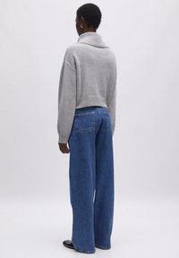 Grijze cropped trui met een brede kraag, gecombineerd met losse blauwe spijkerbroek. Beide stukken hebben een ontspannen pasvorm en zachte texturen.
