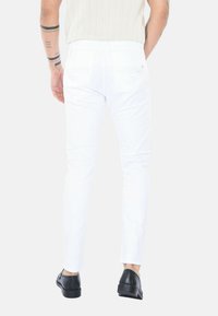 Jeans bianchi slim fit, con tasche posteriori e dettagli di cucitura. Abbinati a scarpe nere. Tessuto liscio, materiale in cotone.