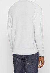 Jasnoszary sweter z dzianiny o prążkowanej fakturze, z długimi rękawami i okrągłym dekoltem. Połączony z ciemnoniebieskimi dżinsami z widocznymi szwami.