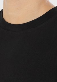 Schwarzes T-Shirt mit Rundhalsausschnitt, glattem Baumwollstoff und figurbetontem Schnitt, der minimale Nähte und einen nahtlosen Kragen betont.