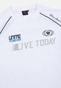 Witte T-shirt met korte mouwen en zwarte accenten, met "UNITE FOREVER" in het rood en blauw, en "LIVE TODAY" in het grijs op de voorkant.