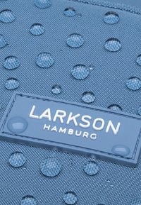 Kék textúrájú szövet vízcseppekkel, a fehér téglalap alakú logóval, ami azt olvassa: "LARKSON HAMBURG". Figyelemre méltó fényes hangsúlyokkal.