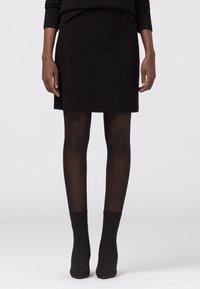 Svart kjol i glat tyg, åtsittande design, midjehöjd, kombinerad med genomskinliga svarta strumpbyxor och svarta klackstövlar i ankellängd.