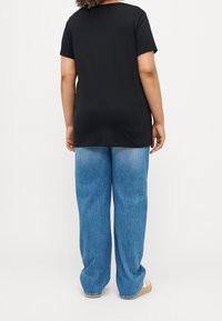 Svart bomull T-shirt med kort ärm, i kombination med ljusblå tvättade denimbyxor med vida ben och vita avslappnade skor.