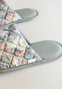 Paplónové papuče s pastelovým kvetinovým vzorom, šedým prešívaným materiálom a mäkkou šedou podšívkou so malou značkovou etikou.