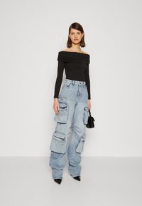 Musthave musta õlalt alla ulatuv pikakäiselise pluusiga, mis on paaritatud helesiniste ülemõõduliste taskute ja tõmblukkudega cargo teksadega ning mustade teravate kontsadega.