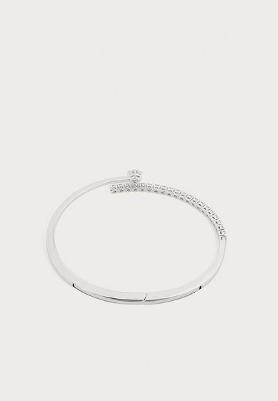 Bracelet ton argent avec une moitié lisse et une moitié sertie de petites pierres claires, présentant un petit détail de couronne sur fond blanc.