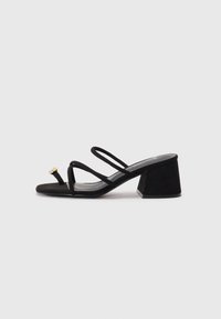 Sandalias negras de tacón cuadrado con puntera cuadrada, tiras delgadas y un pequeño detalle decorativo. Fabricadas con un material de ante suave.