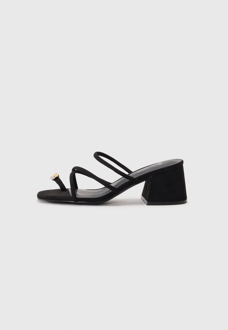 Sandalias negras de tacón cuadrado con puntera cuadrada, tiras delgadas y un pequeño detalle decorativo. Fabricadas con un material de ante suave.