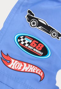 Un patch en tissu bleu avec trois autocollants en vinyle : une silhouette de voiture de course noire, un logo Hot Wheels arrondi et un logo en forme de flamme.