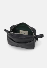 Borsa nera in pelle con chiusura a zip, caratterizzata da un interno in tessuto verde e un'etichetta con il marchio. Include una maniglia laterale e dettagli di cucitura sottili.