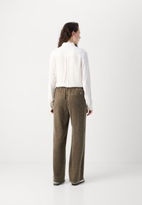 Lange, loszittende bruine patroonbroeken met een elastische tailleband, gecombineerd met een witte geribbelde shirt met een achterste naad.