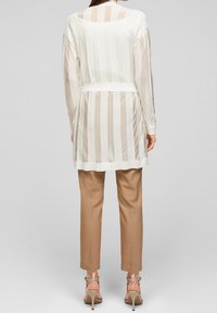 Lekki, przezroczysty biały kardigan z pionowymi paskami, przewiązany w talii. Połączony z beżowymi, dopasowanymi spodniami i sandałami na obcasach.