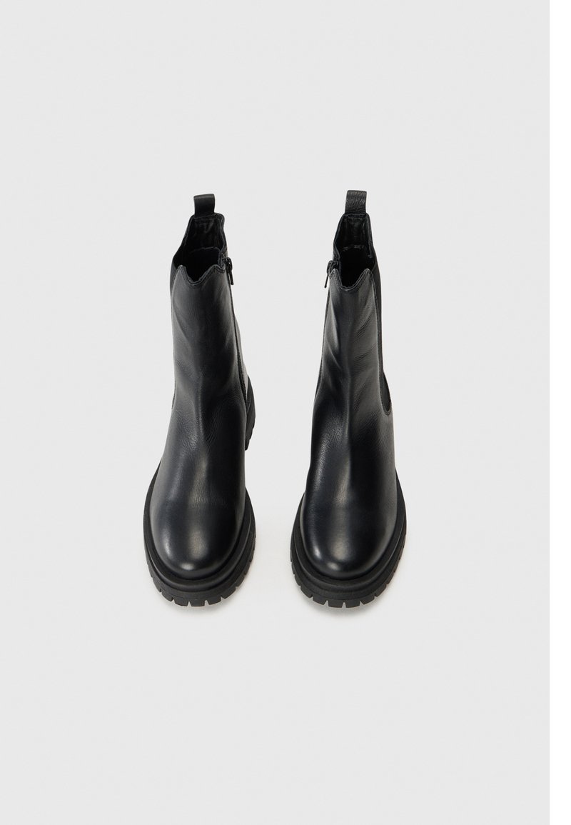 Schwarze Lederstiefeletten mit glatter Textur und abgerundeter Zehenform, ausgestattet mit einer niedrigen, klobigen Sohle und einer Schlaufe an der Rückseite für ein einfaches An- und Ausziehen.