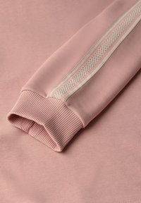 Manga de sudadera rosa con puño acanalado, que presenta un acento lateral de tejido de malla y una franja texturizada. Material suave y liso.