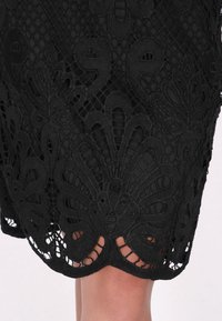 Abito in pizzo nero con ricami floreali intricati e motivi geometrici, con orlo a scallop e texture trasparente.