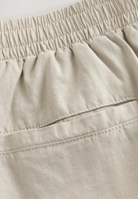 Beige linnedren shorts med en sammendraget elastisk talje og en enkelt baglomme med synlig stikning og blød tekstur.