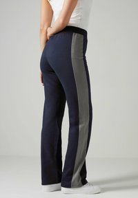 Marineblauwe sweatpants met grijze zijpanelen, voorzien van een elastische tailleband en een relaxte pasvorm, gecombineerd met witte sneakers.